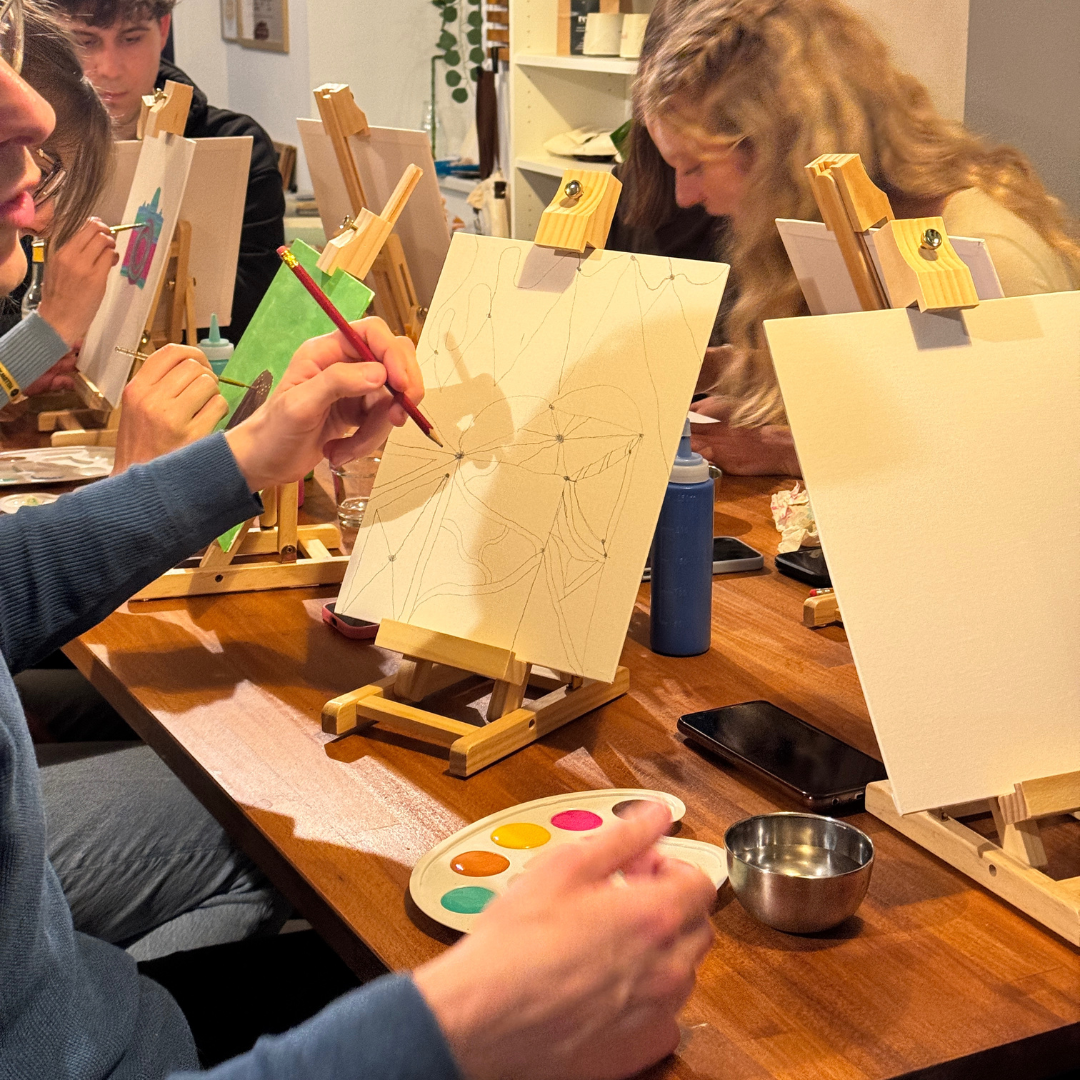 People painting at a table with easels and art supplies