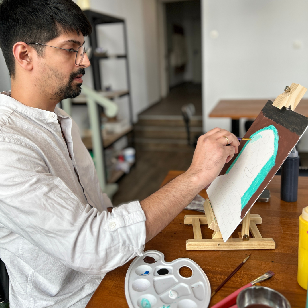 Man painting on a canvas with a palette and brushes in a studio setting