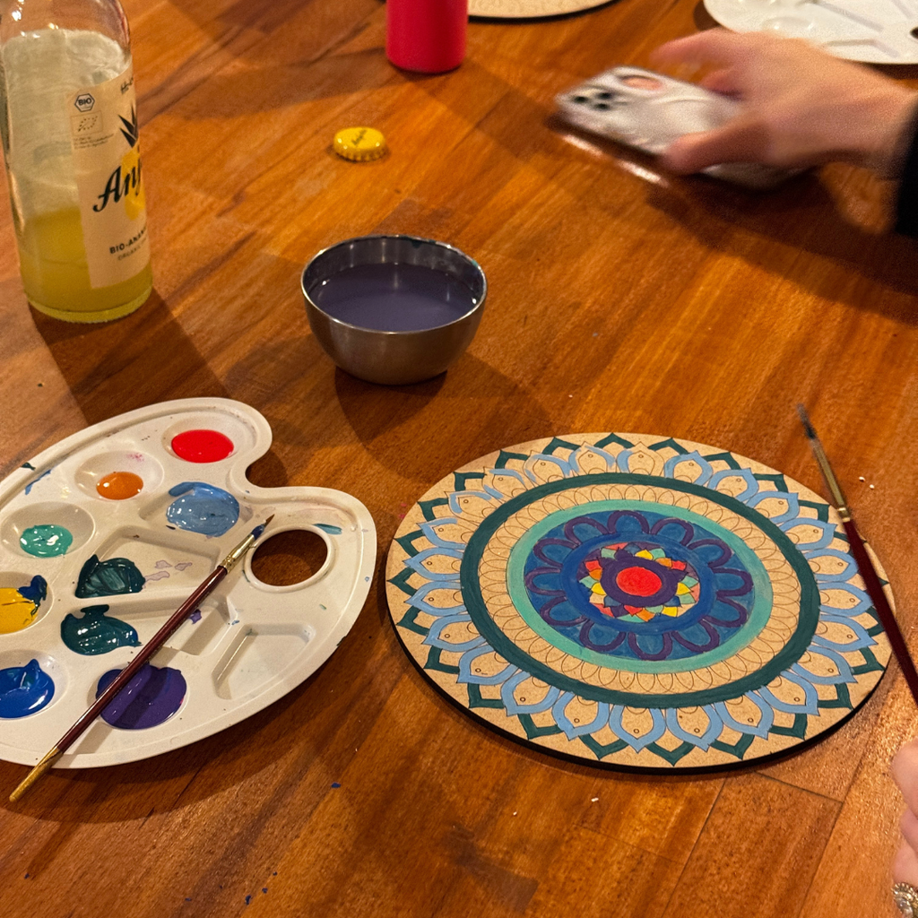 Colorful mandala on a wooden table with art supplies and a bottle of juice.