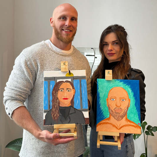 Two people holding paintings of themselves